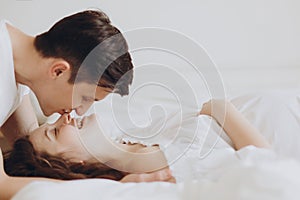 Happy pregnant couple relaxing on white bed and holding belly bump. Happy young husband kissing his smiling wife and hugging baby