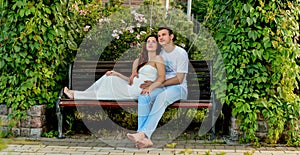 Happy pregnant couple sitting on the banch in park