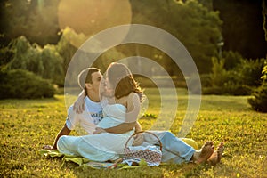 Happy pregnant couple sitting on the grass in park