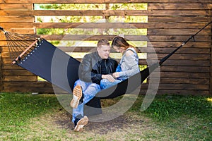 Happy pregnant couple sitting in hammock - family, parenthood and happiness concept