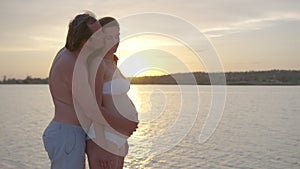 Happy pregnant couple together at sunset husband embracing wife gently holding her belly enjoying.