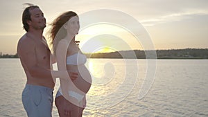 Happy pregnant couple together at sunset husband embracing wife gently holding her belly enjoying.