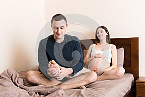 Happy pregnant family. Husband massaging his pregnant wife legs and sitting together on couch in their home