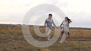 Happy pregnant family walks in a field at sunset, a man holding his wife's hand