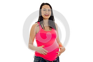 Happy pregnant future mother in pink shirt touching her belly isolated on white background