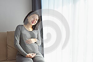 Happy Pregnant lady looking through a window sitting at home with copy space