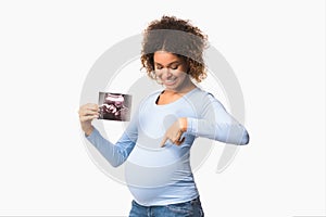 Happy pregnant lady showing ultrasound scans and pointing at belly