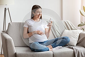 Happy pregnant millennial woman using smartphone at home, browsing pregnancy app