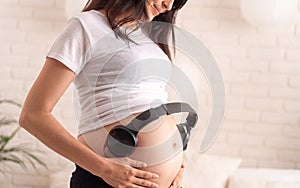 Happy pregnant mom with bare stomach, enjoying listening to music in headphones