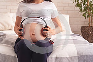 Happy pregnant mom with bare stomach, enjoying listening to music in headphones