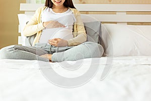 Happy pregnant mother touching beautiful belly sitting on cozy bed at home. prenatal, pregnancy, motherhood, expect concept. Young