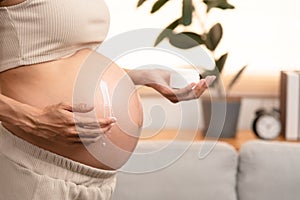 Happy pregnant woman apply skincare cream lotion on pregnant belly to prevent stretch mark. Healthy skin massage treatment and