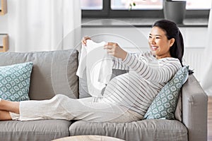 happy pregnant woman with baby& x27;s bodysuit at home