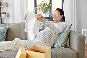 happy pregnant woman with baby& x27;s bodysuit at home