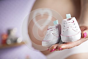 Happy pregnant woman, baby shoes in her hands