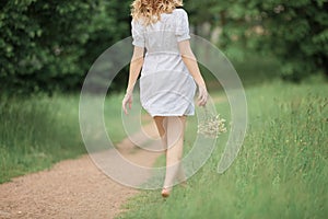 Happy pregnant woman with a bouquet walking barefoot on the grass