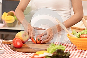Happy pregnant woman cooking at home, preparing fresh green salad, eating many different vegetables good for pregnancy, healthy