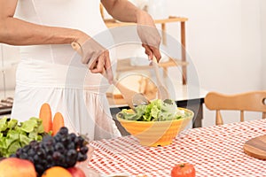 Happy pregnant woman cooking at home, preparing fresh green salad and fruit, eating many different vegetables good for pregnancy,