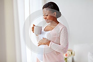 Happy pregnant woman with cup drinking tea at home