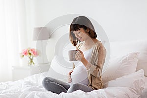 Happy pregnant woman with cup drinking tea at home