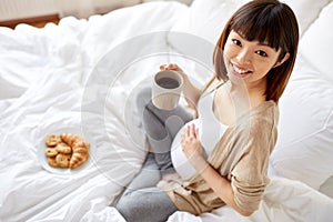 Happy pregnant woman with cup drinking tea at home