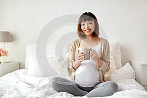 Happy pregnant woman with cup drinking tea at home