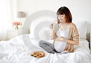 Happy pregnant woman with cup drinking tea at home