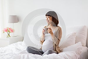 Happy pregnant woman with cup drinking tea at home