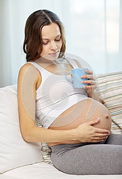 Happy pregnant woman with cup drinking tea at home