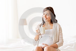 Happy pregnant woman with cup drinking tea at home