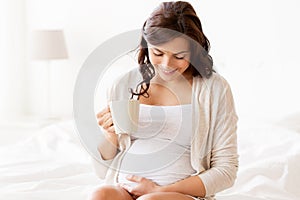 Happy pregnant woman with cup drinking tea at home