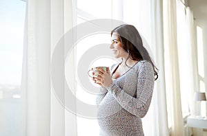 Happy pregnant woman with cup drinking tea at home