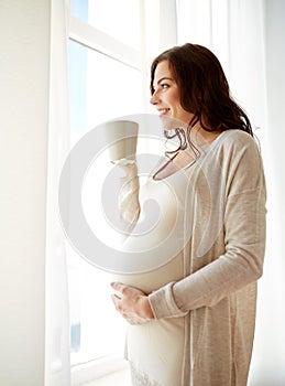 Happy pregnant woman with cup drinking tea at home