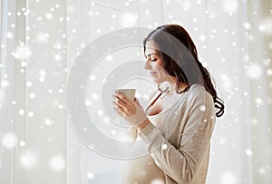 Happy pregnant woman with cup drinking tea at home