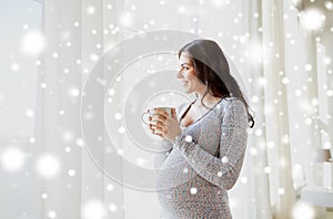 Happy pregnant woman with cup drinking tea at home