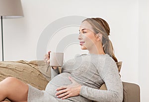 Happy pregnant woman with cup drinking tea at home