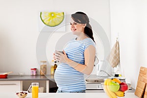 Happy pregnant woman with cup at home kitchen