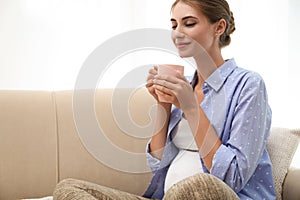 Happy pregnant woman drinking tea at home