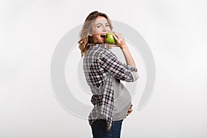 happy pregnant woman eating apple and smiling at camera