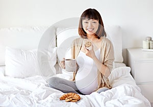 Happy pregnant woman eating cookie in bed at home
