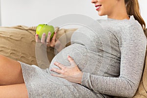 Happy pregnant woman eating green apple at home