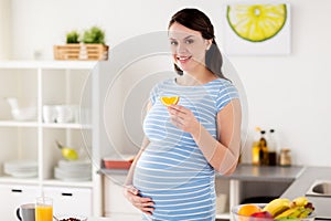 Happy pregnant woman eating orange at home