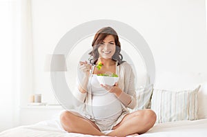 Happy pregnant woman eating salad at home