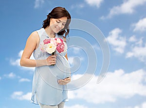 Happy pregnant woman with flowers touching belly