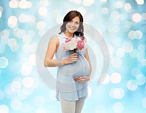 Happy pregnant woman with flowers touching belly