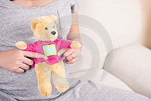 Happy pregnant woman hand holding teddy bear doll on her belly w