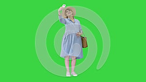 Happy pregnant woman in a hat using her smartphone doing selfie on a Green Screen, Chroma Key.