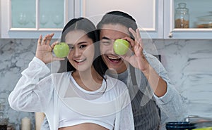 Happy pregnant woman and her handsome husband holding apple on eyes in the kitchen at home. Healthy food concept