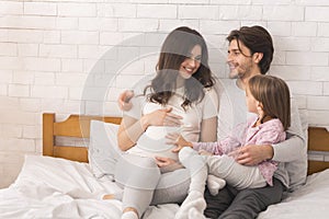 Happy Pregnant Woman, Her Husband And Daughter Lying Together In Bed