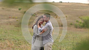 Happy pregnant woman with her husband in a field near a big tree.